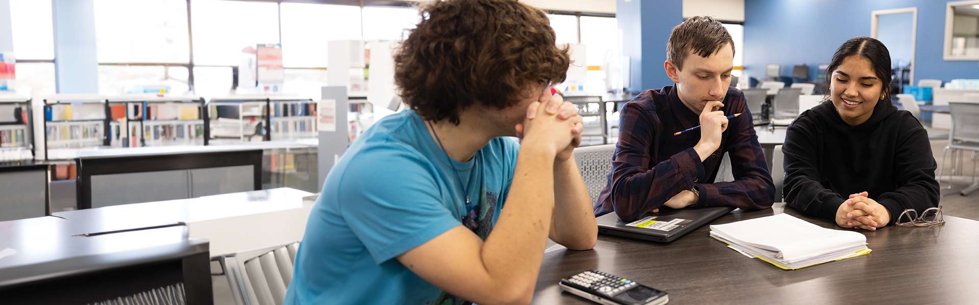 Three college students sitting at a table in a library and studying together.