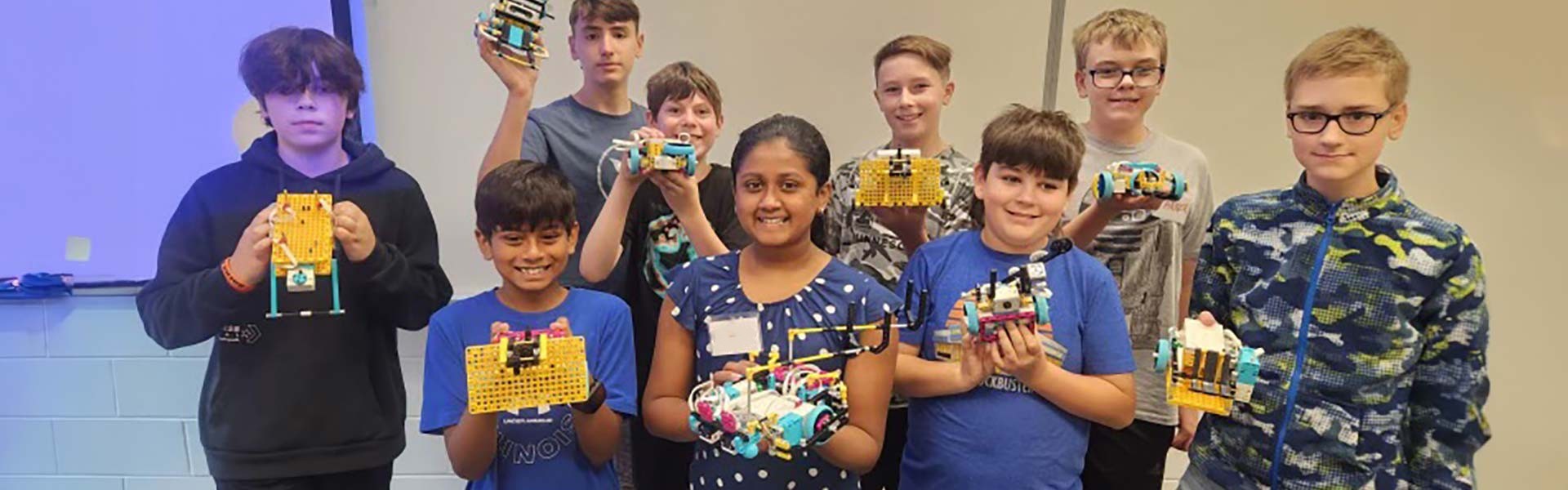 Nine summer camp participants, including one female and eight male middle schoolers, holding up their LEGO robotics projects.